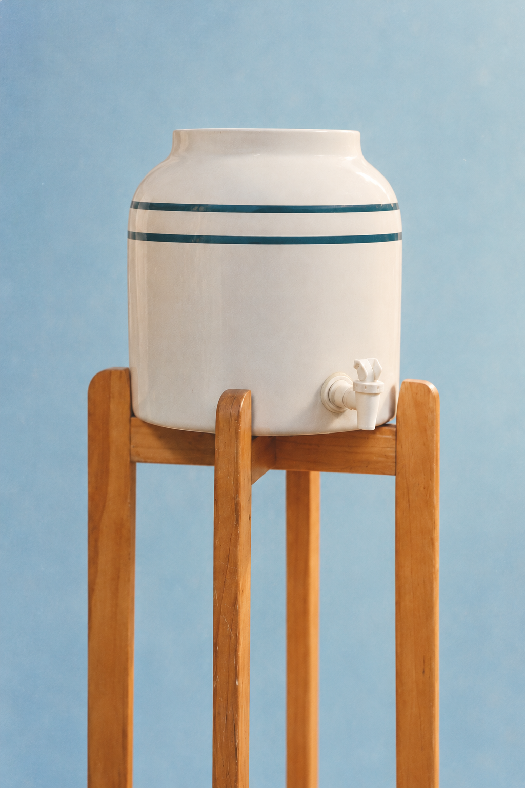 Cream ceramic tea dispenser on a wooden stand against a blue backdrop
