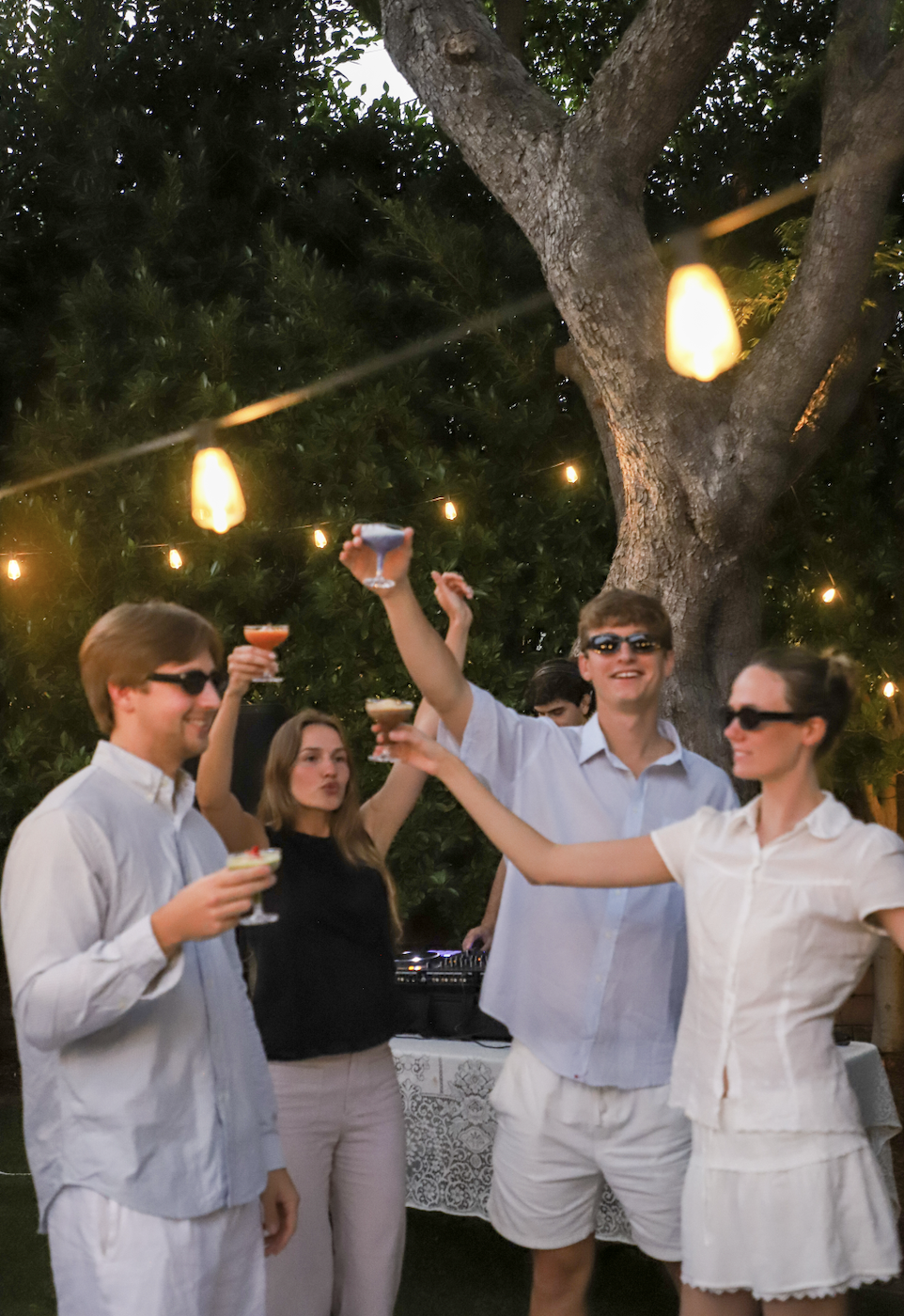 Guests raising colorful Fogato cocktails in a toast at a private celebration under string lights